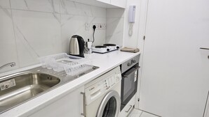 A kitchen with a stainless steel sink, a Bosch washing machine, a coffee maker, and a stove. - 109 LIM 1 - Stay Olive Studio (Limassol)
