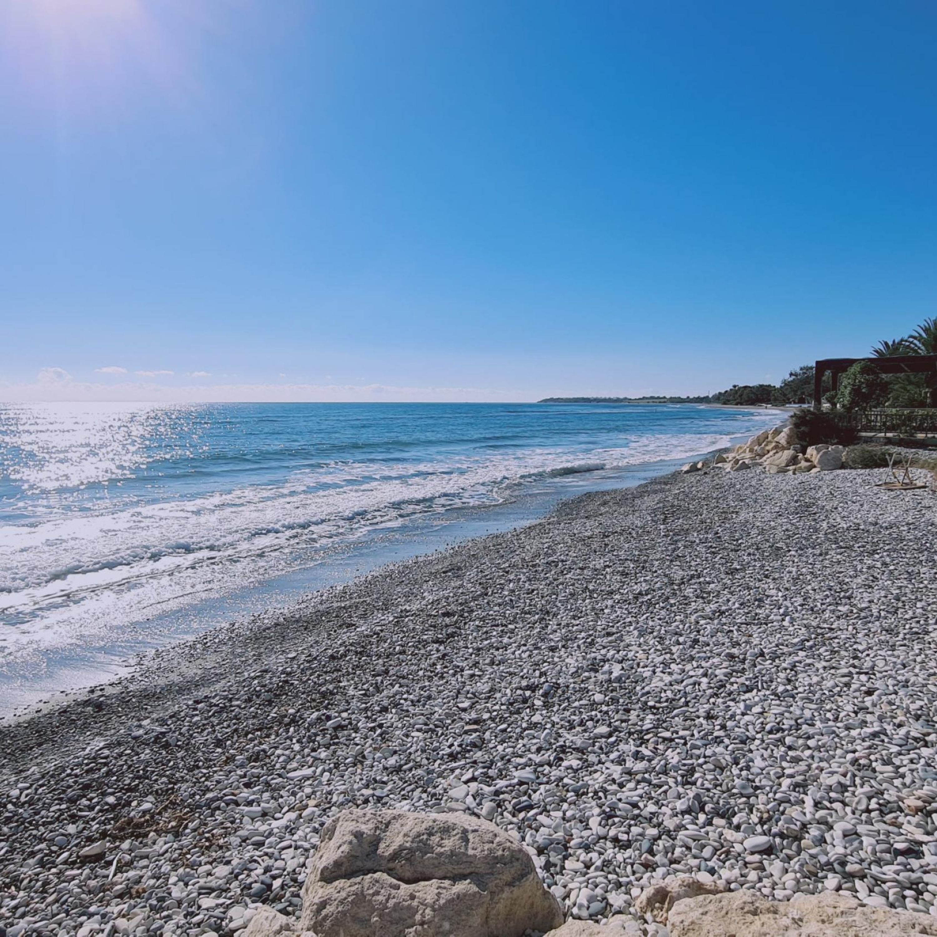 Ein Kiesstrand mit felsiger Küstenlinie und blauem Himmel.