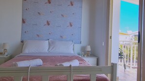 A bedroom with a bed, bedside tables, a window, and a view of the outside. - 10 MEN - Stay Crystal Waves Maisonette (Meneou)