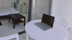 A modern hotel room with a bed, a small table, a laptop on a chair, and a view of the kitchen and balcony. - 109 LIM 3 - Stay Terra Cota Studio (Limassol)