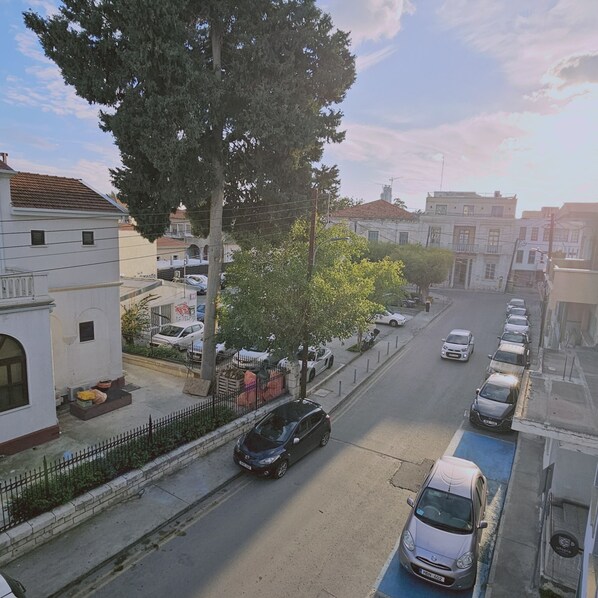 Vista de la calle con coches aparcados, aceras arboladas y edificios con balcones.