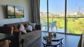 A living room with a sofa, TV, and a balcony with chairs and a table. - 30 PRO - Stay White Coral Studio (Paralimni)
