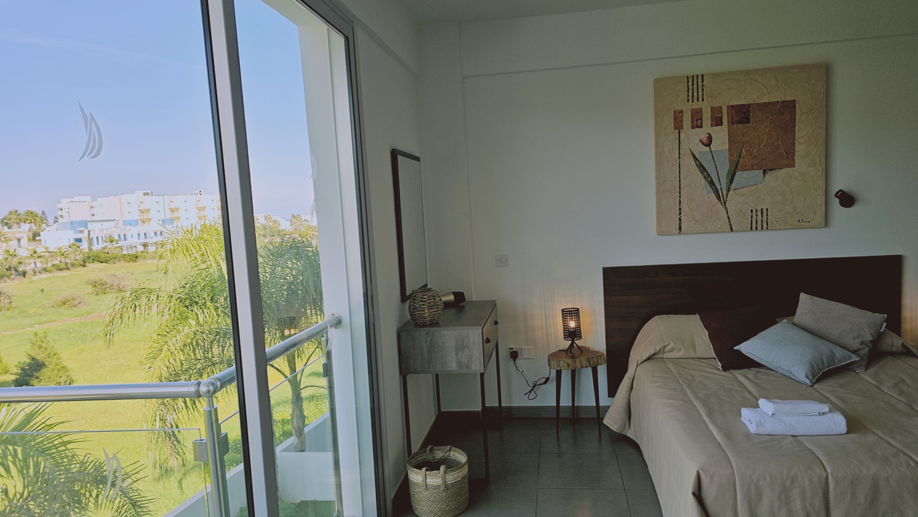 Una habitació d'hotel amb un finestral gran, un llit, una taula de nit amb una làmpada i un quadre a la paret.