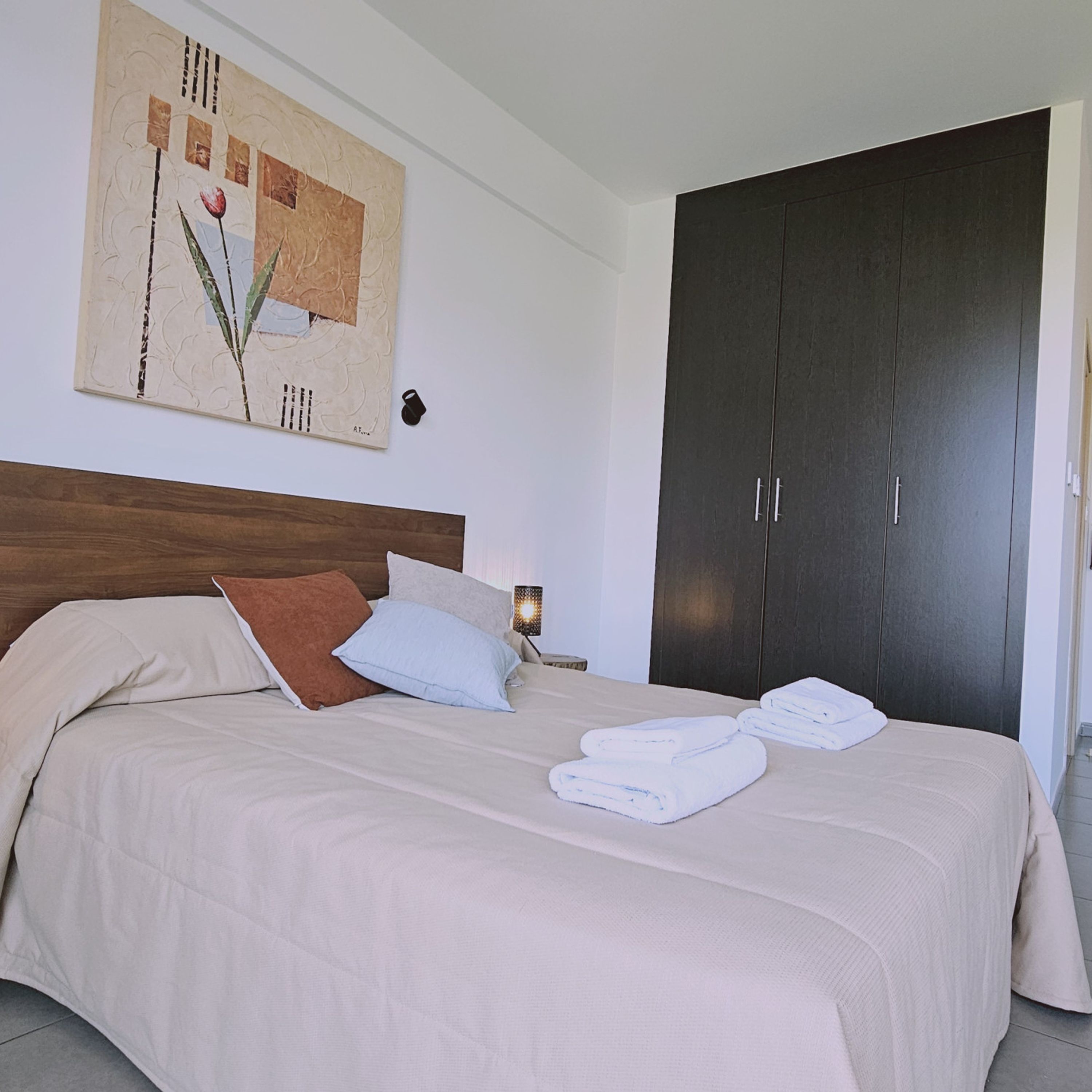 Ein Schlafzimmer mit einem Bett, Kissen, einem Nachttisch, einer Lampe und einem dunklen Wandschrank.