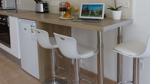 A modern kitchen with white cabinets, a microwave, a coffee maker, a laptop on the counter, and a potted plant. - 112 AN - Stay Paradise Sands Studio (Ayia Napa)