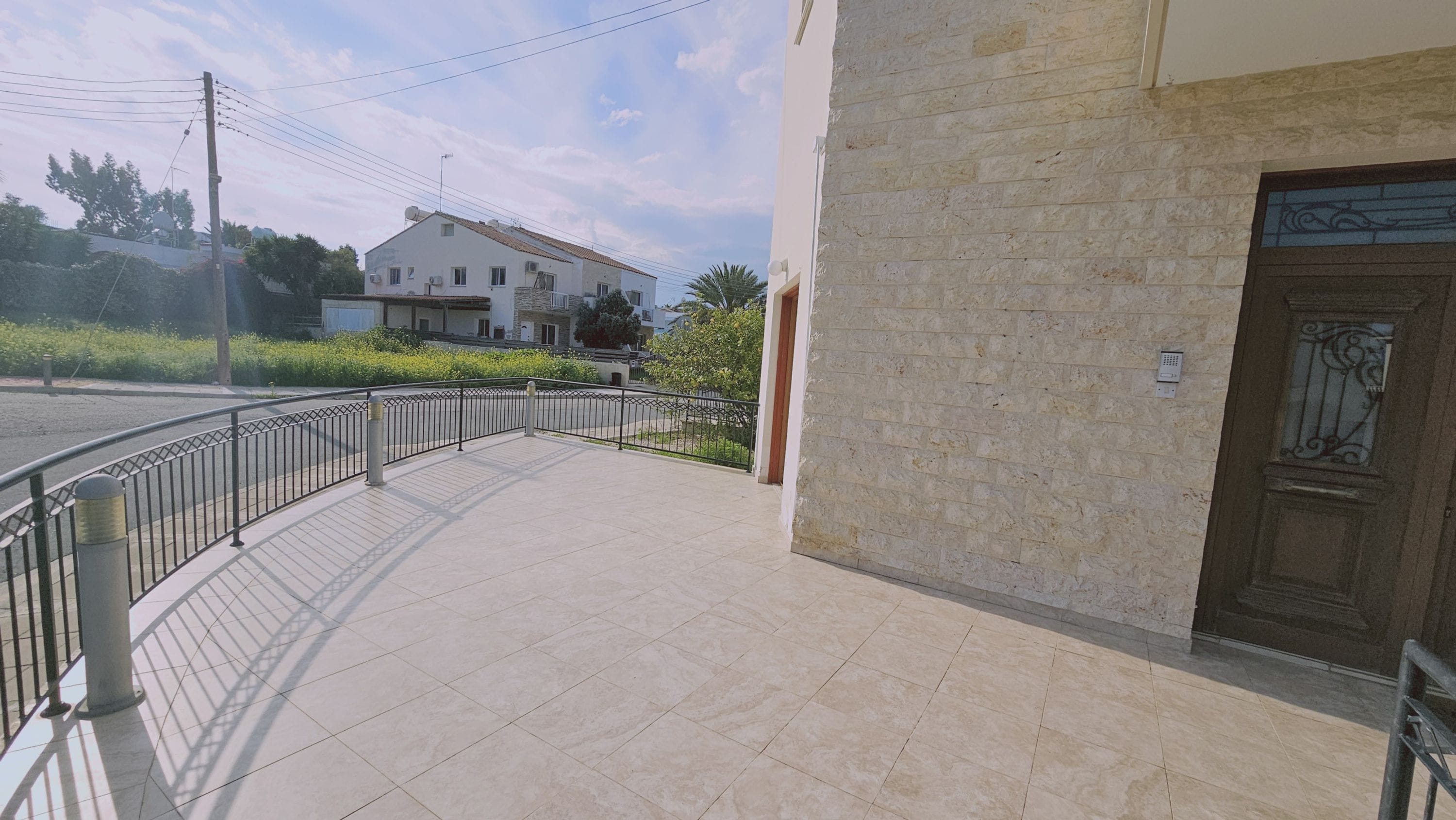 A paved walkway with a metal railing, a building entrance with a decorative door, and a residential building in the background.