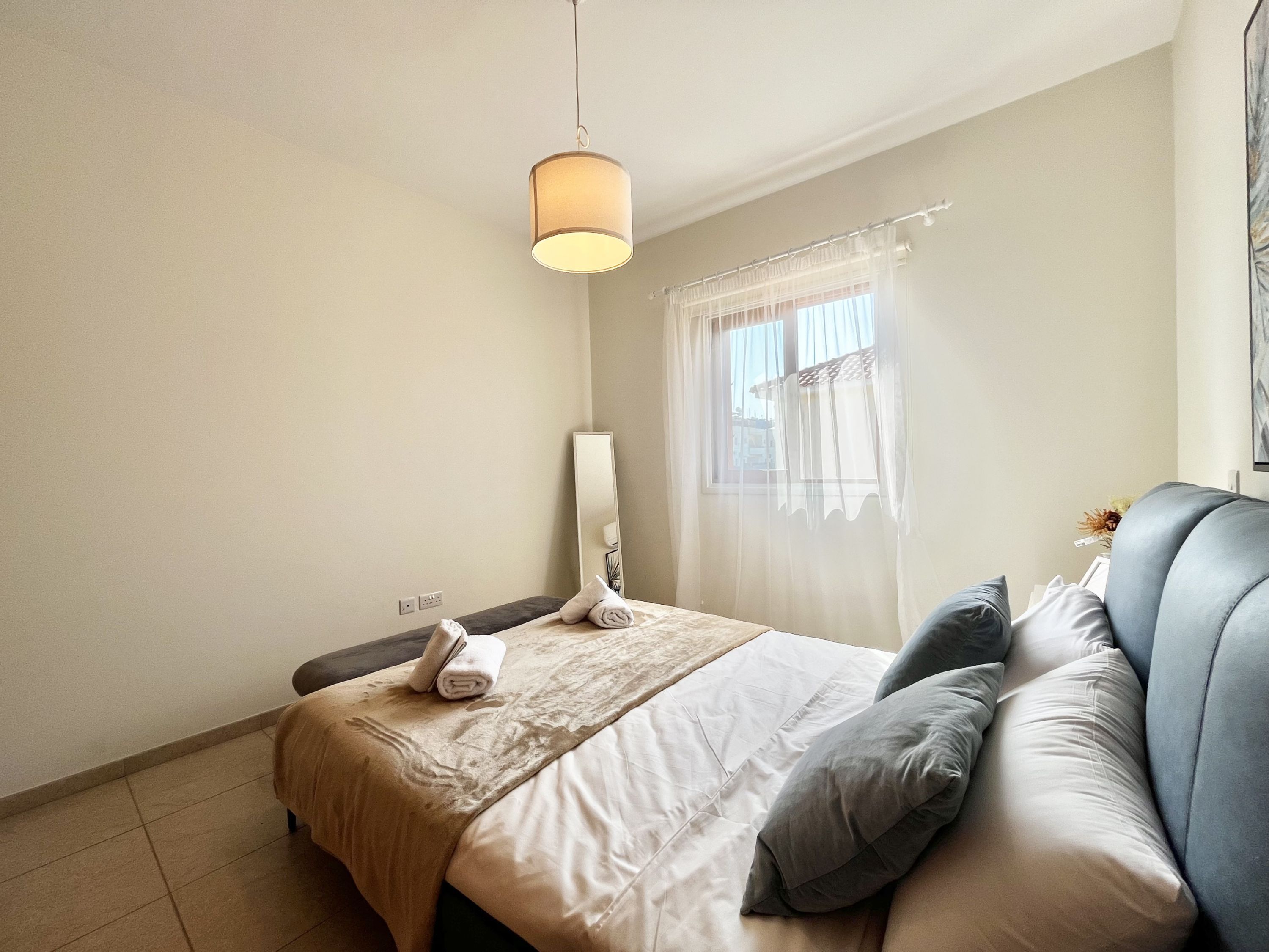 A bedroom with a bed, a bedside table, a lamp, and a window with curtains.