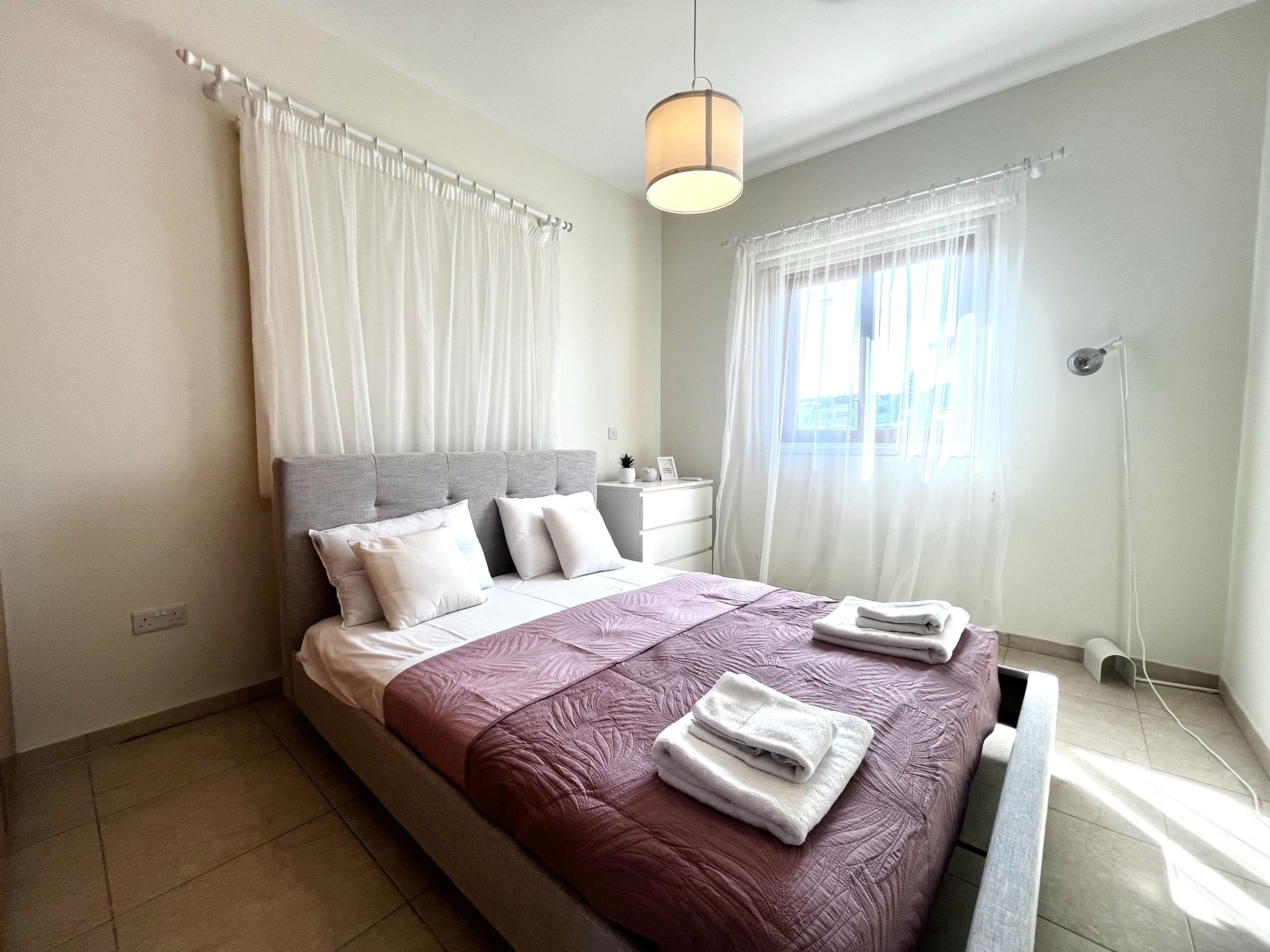 A modern bedroom with a large bed, a bedside table, and a window with curtains.