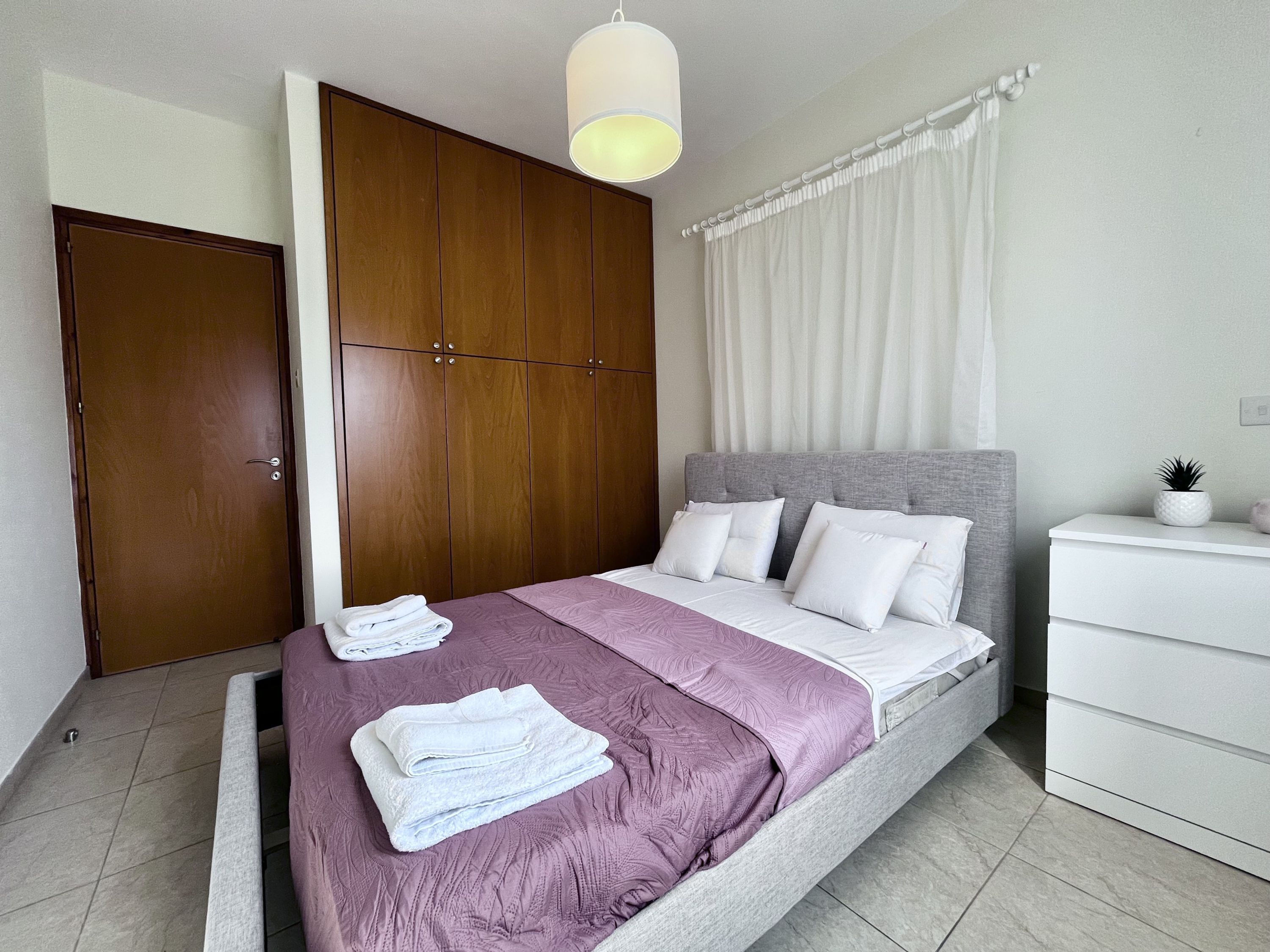 Un dormitorio con cama, armario, mesita de noche y lámpara colgante.