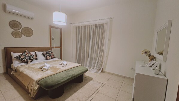 A hotel room with a bed, a bedside table, a mirror, a window with curtains, and an air conditioning unit. - 111 VOR - Stay Tranquility Cove (Oroklini)