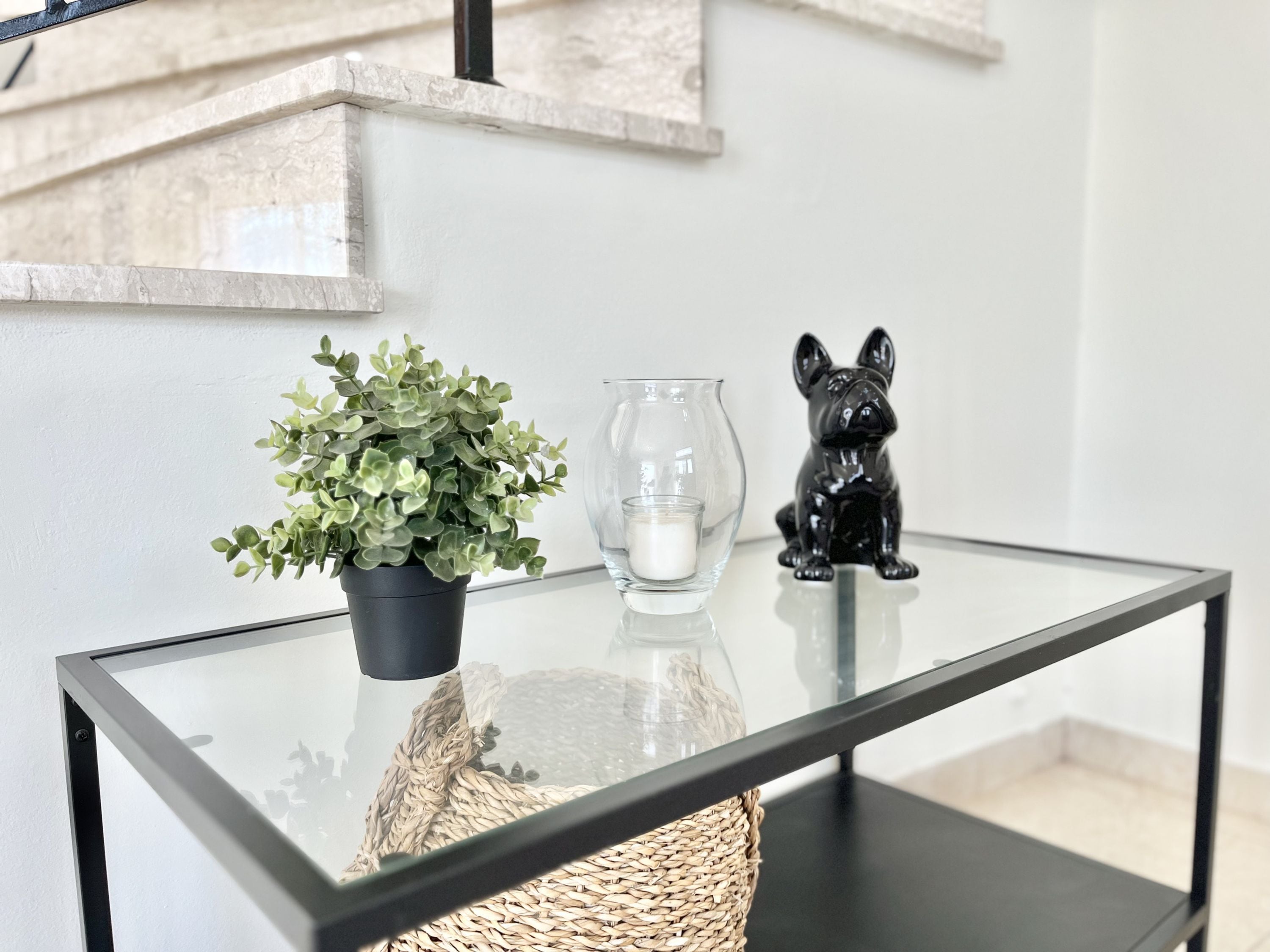 Ein Tisch mit Glasplatte, ein Blumentopf, eine Kerze und eine Figur.