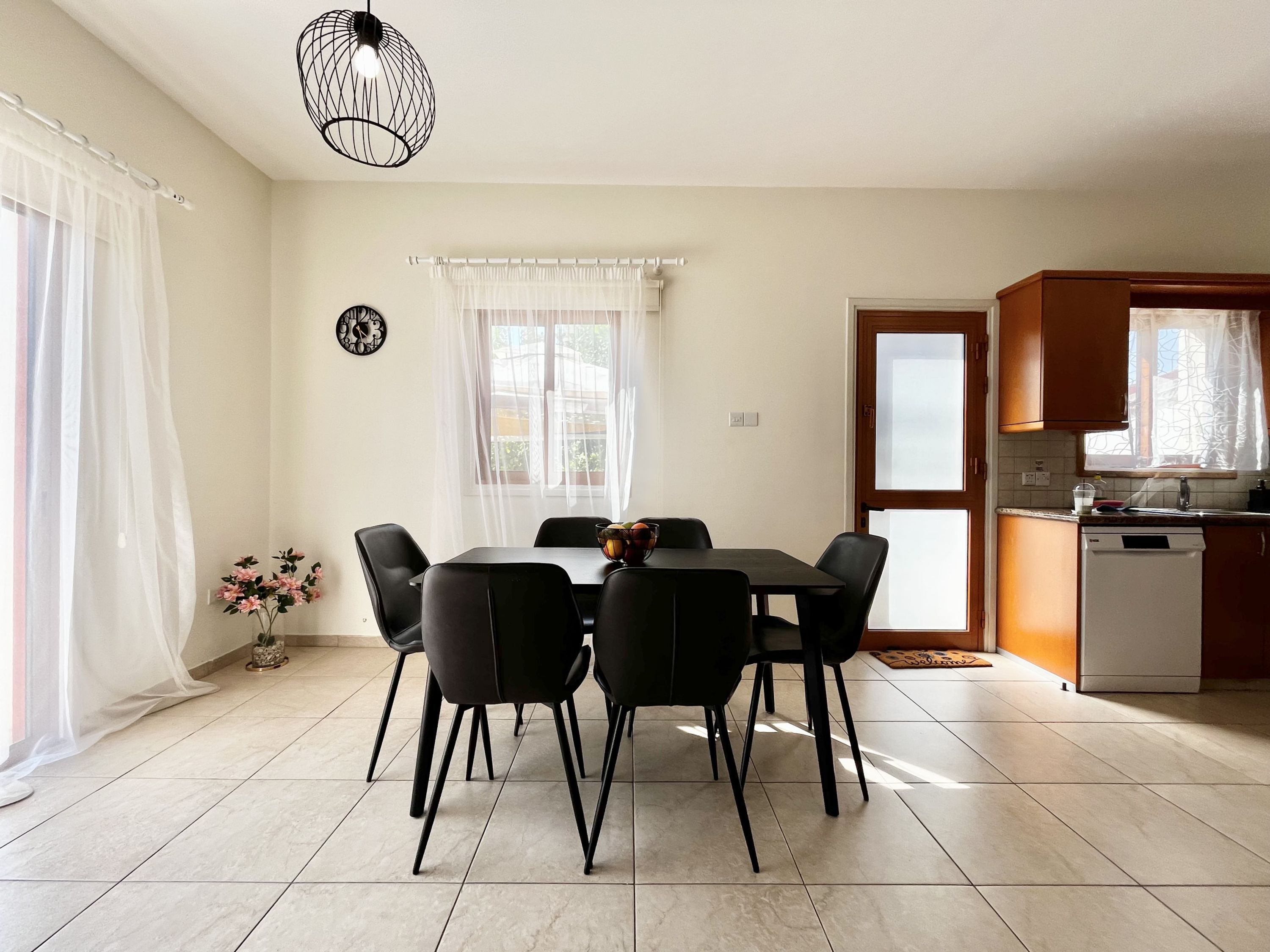 A dining area with a table and chairs, a kitchen with a dishwasher, and a window with curtains.