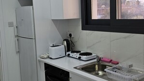 Una cucina compatta con mobili bianchi, forno integrato, tostapane, bollitore e una finestra con vista sulla città.