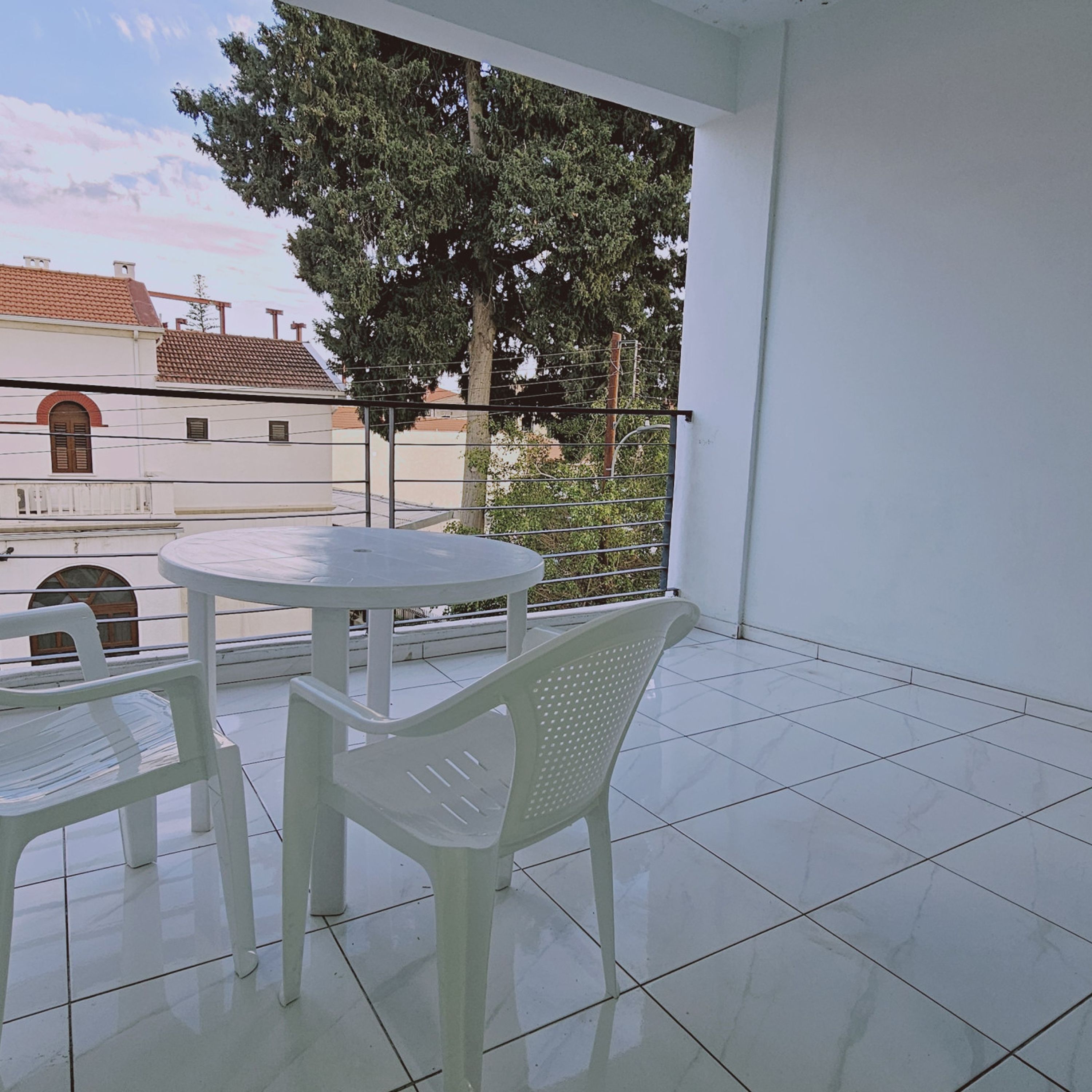 A balcony with a white table and chairs, a view of a tree, and a building in the background.