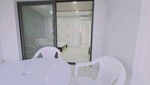 Una stanza con una porta scorrevole in vetro che dà su un bagno, un tavolo bianco con sedie e un pavimento piastrellato.