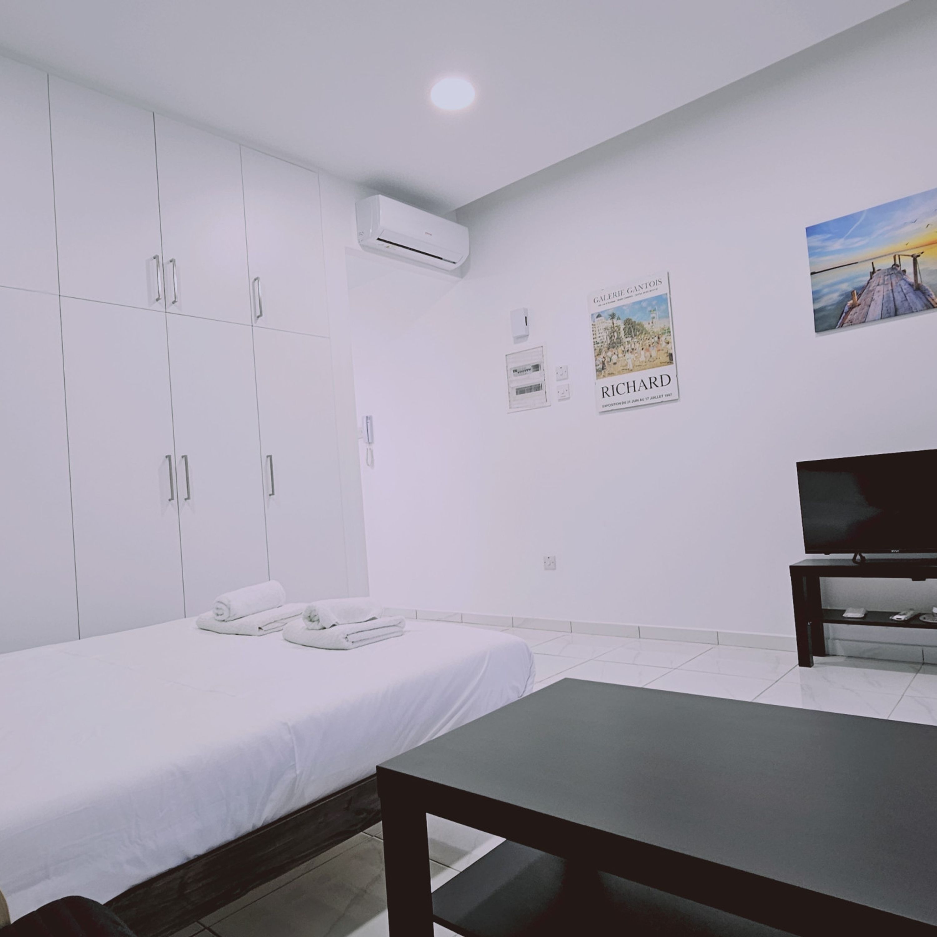 Une chambre moderne avec un lit, une télévision et un bureau. On y trouve des armoires blanches et un tableau accroché au mur.
