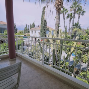 A balcony with a metal railing, a bench, and a view of a house and cacti. - 122 VOR - Stay Cactus House (Oroklini)