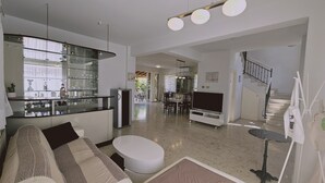 A modern living room with a sofa, a dining table, and a kitchen area with a refrigerator and glass cabinets. - 122 VOR - Stay Cactus House (Oroklini)