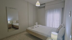 A bedroom with a bed, a bedside table with a lamp, a mirror, and a window with curtains. - 126 NIC - Stay Incity Apartment (Nicosia)