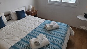 A bedroom with a bed, a nightstand, a window with a view of the sea, and a small table with a plant. - 119 LCA - Stay Dreamy Seaside Apartment (Larnaca)