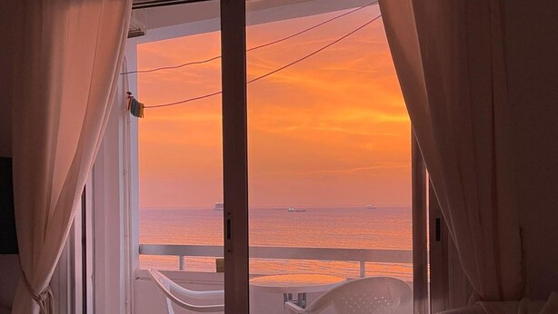 A room with a view of the sea at sunset, featuring a balcony with a table and chairs. - 119 LCA - Stay Dreamy Seaside Apartment (Larnaca)