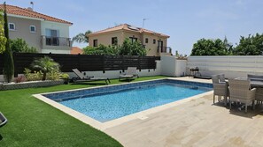 A rectangular swimming pool with a tiled edge, surrounded by a patio area with outdoor furniture.