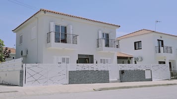 Two-story residence with a balcony and red-tiled roof, featuring a secure entrance and air conditioning units.
