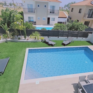 A swimming pool with a tiled deck, surrounded by a grassy area and a wooden fence.