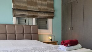 A neatly made bed with a patterned bedspread, a headboard, a bedside lamp, and a rolled towel on the side. - 131 VOR - Stay M L Villa (Oroklini)