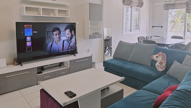 A modern living room with a flat-screen TV, a sofa, a coffee table, and a dining area in the background. - 131 VOR - Stay M L Villa (Oroklini)