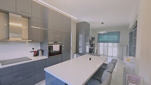 A modern kitchen with a central island, built-in appliances, and a dining area with a bench. - 131 VOR - Stay M L Villa (Oroklini)