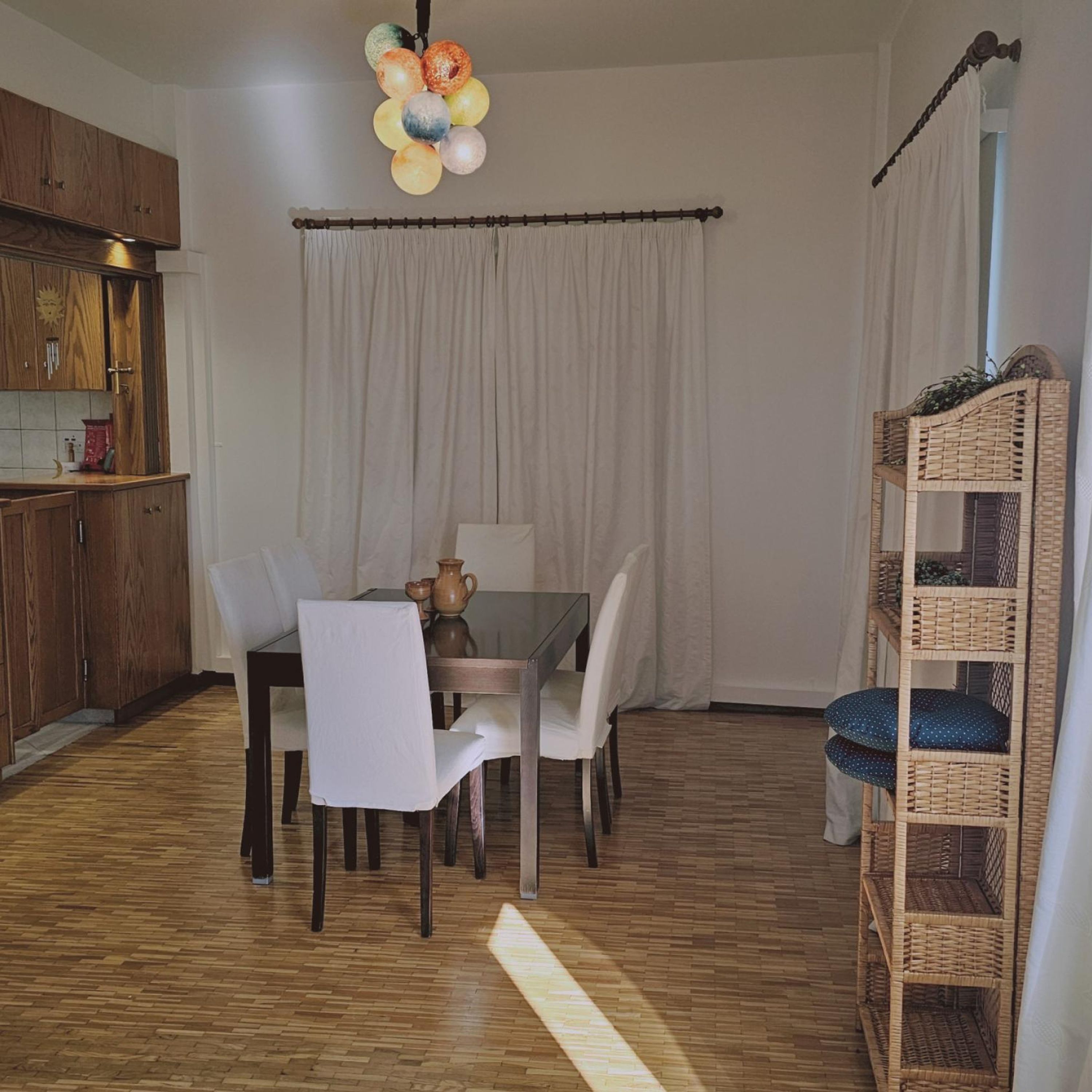Uma sala de jantar com mesa e cadeiras de madeira, luminária pendente e estante de vime.