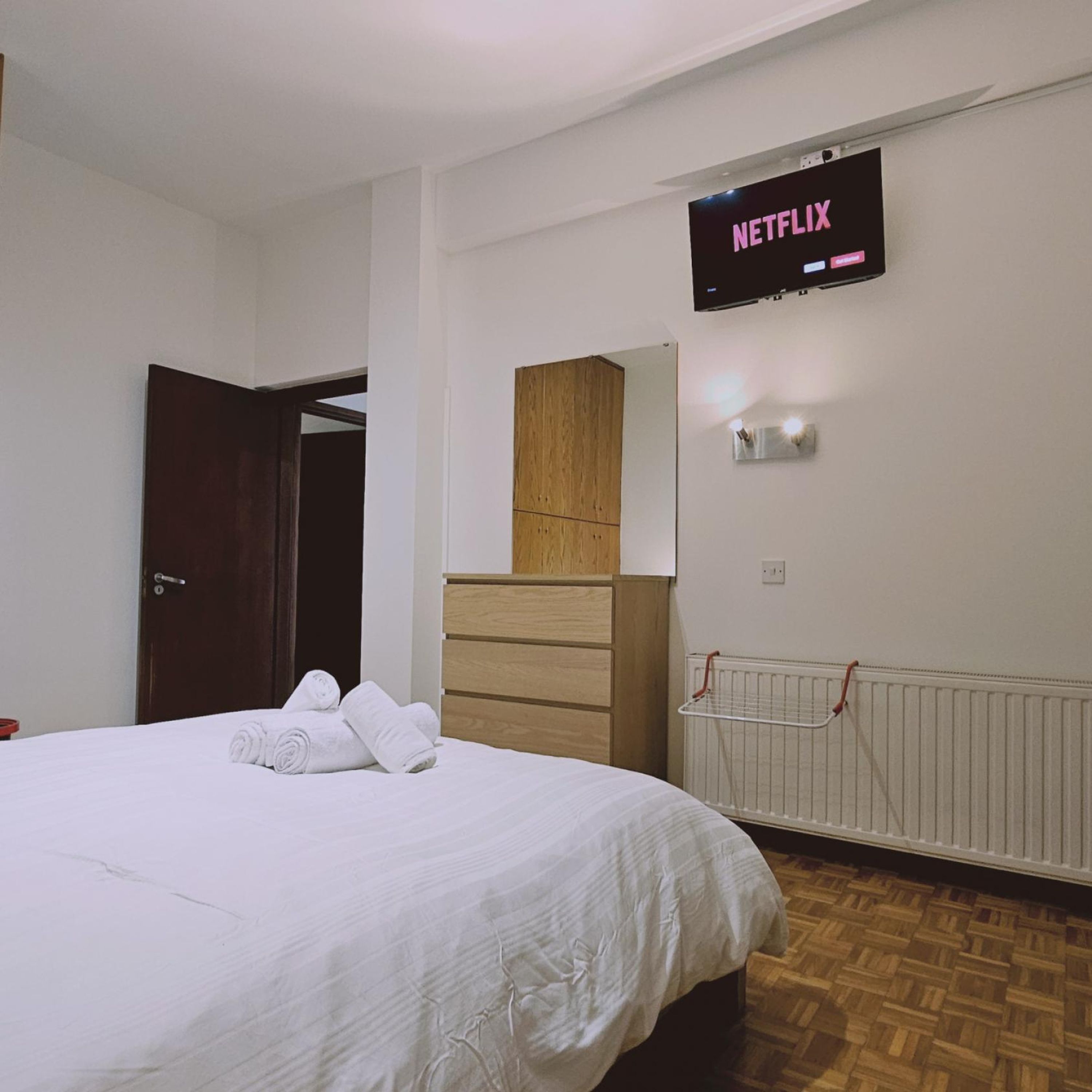 Habitación de hotel con una cama, un armario de madera, un televisor de pared mostrando 'NETFLIX' y un radiador.