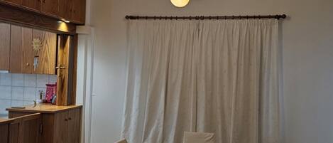 A dining area with a table and chairs, a kitchen with wooden cabinets, and a curtain.
