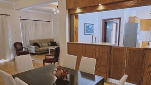 Un coin repas avec une table et des chaises en bois, une cuisine avec des meubles en bois et un salon avec un canapé et des rideaux.