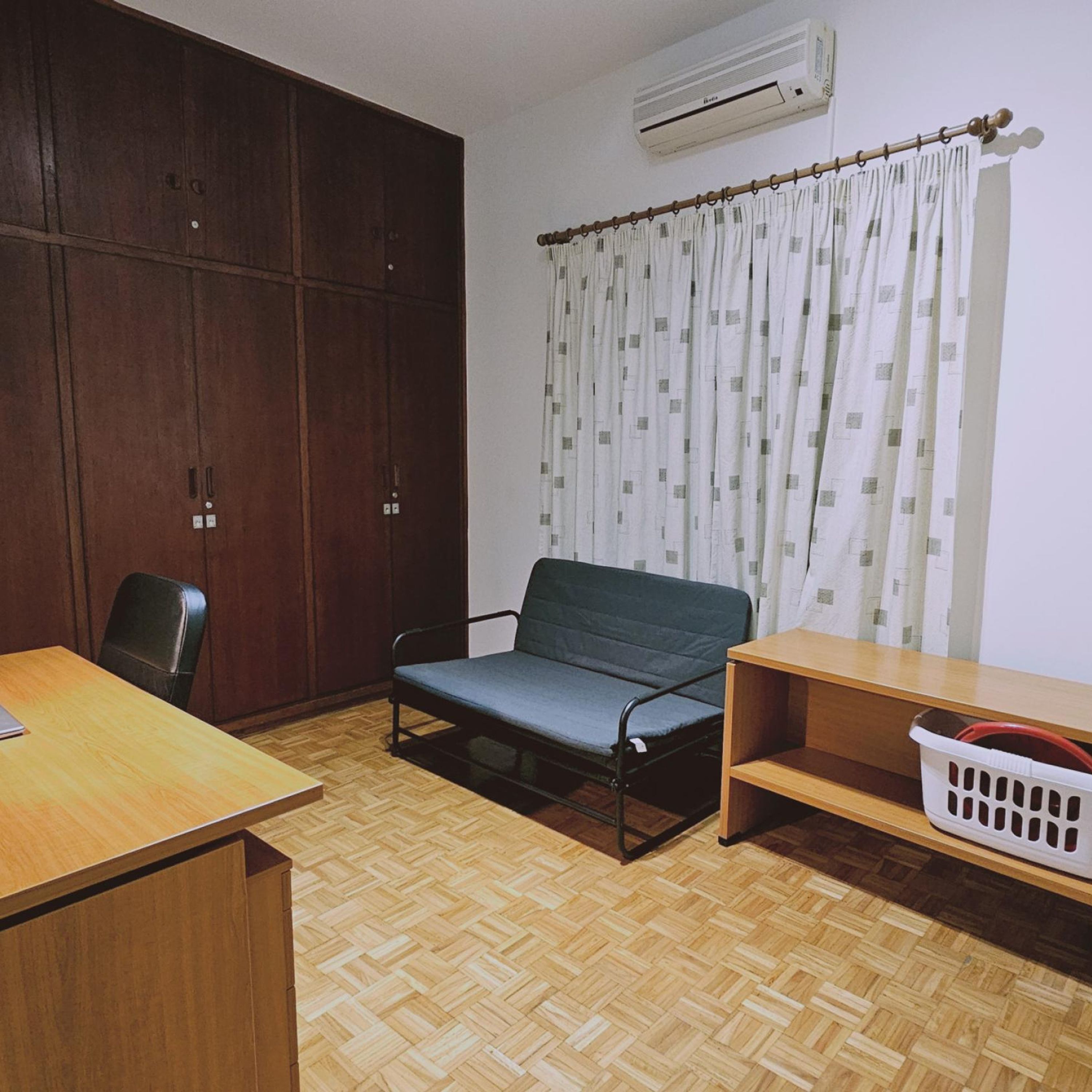 A room with a wooden floor, a bed, a desk, a chair, a wardrobe, and a window with curtains.