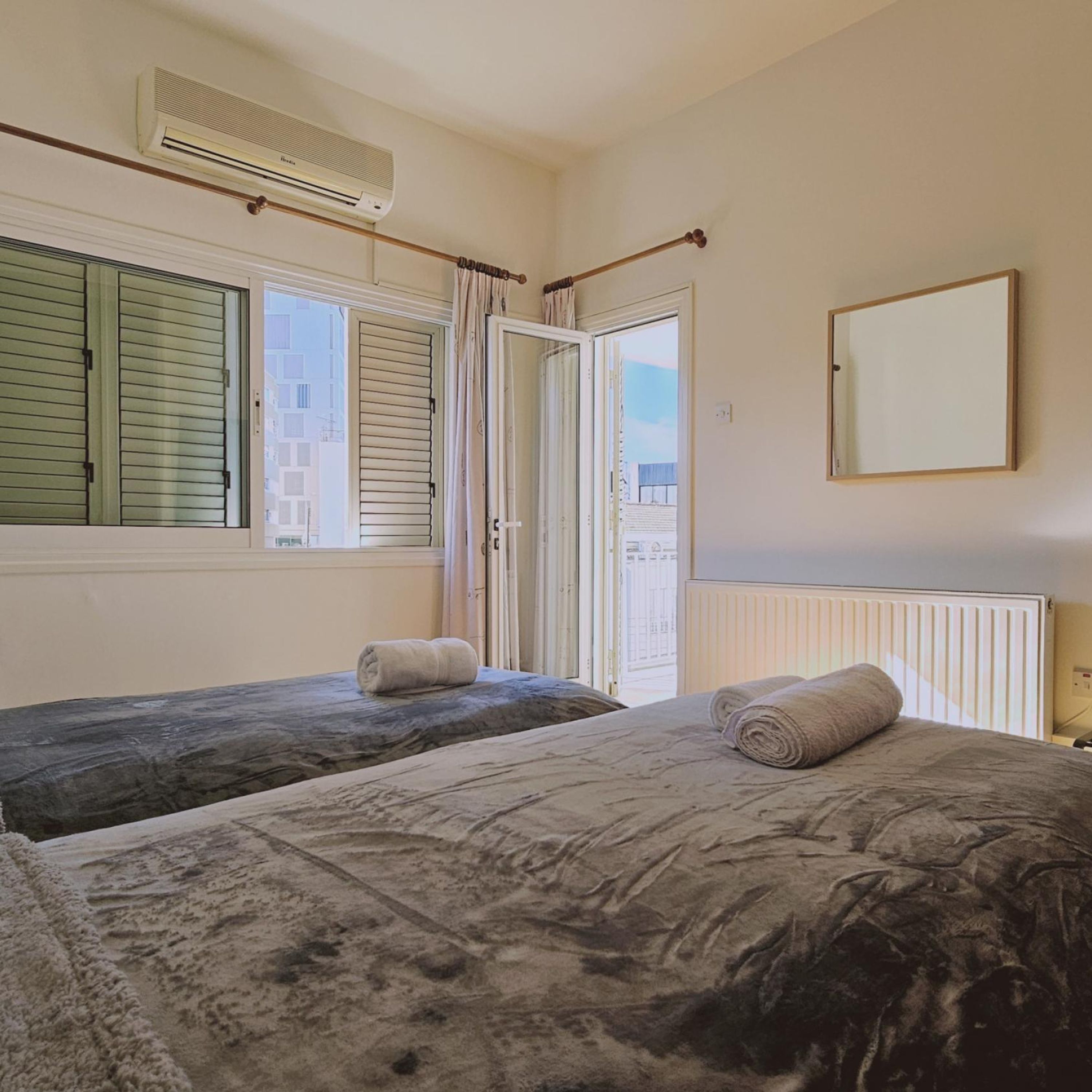 Ein Schlafzimmer mit zwei Betten, einem Fenster mit Rollläden, einem Heizkörper und einem Spiegel an der Wand.