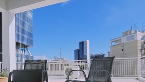 Un balcon avec une table et deux chaises, donnant sur un paysage urbain avec des bâtiments modernes.