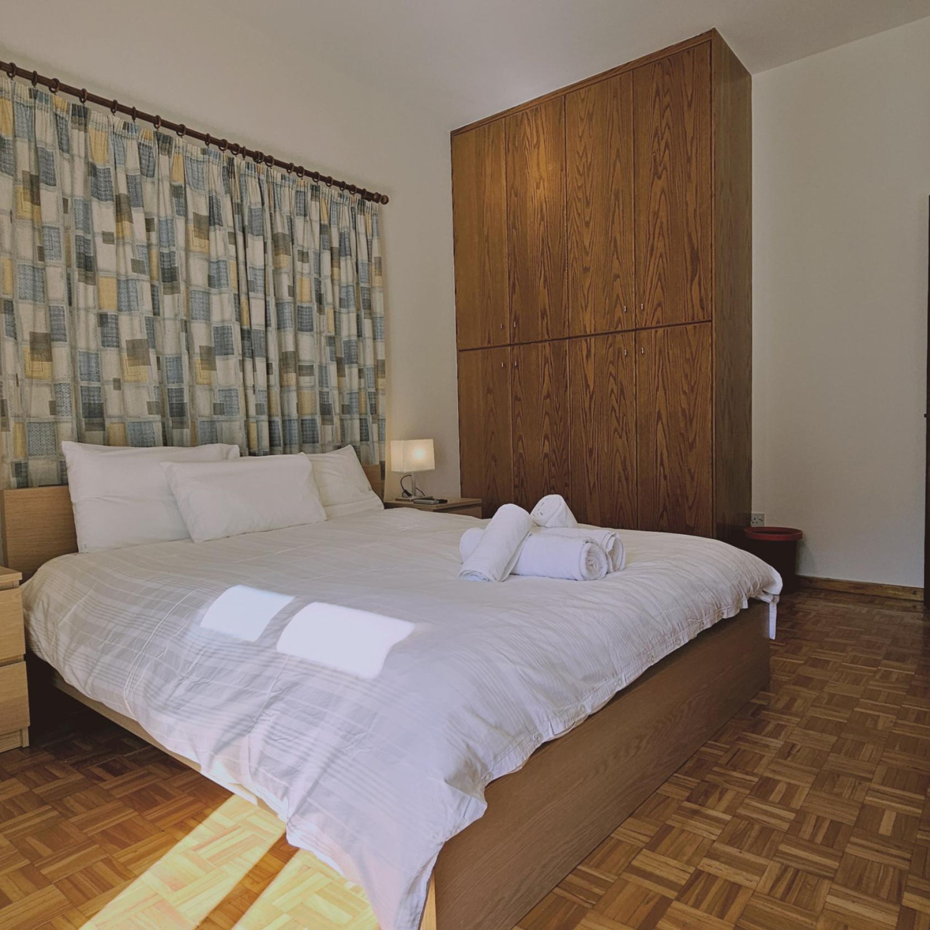 Une chambre d’hôtel avec un grand lit, une armoire en bois et un rideau à carreaux.