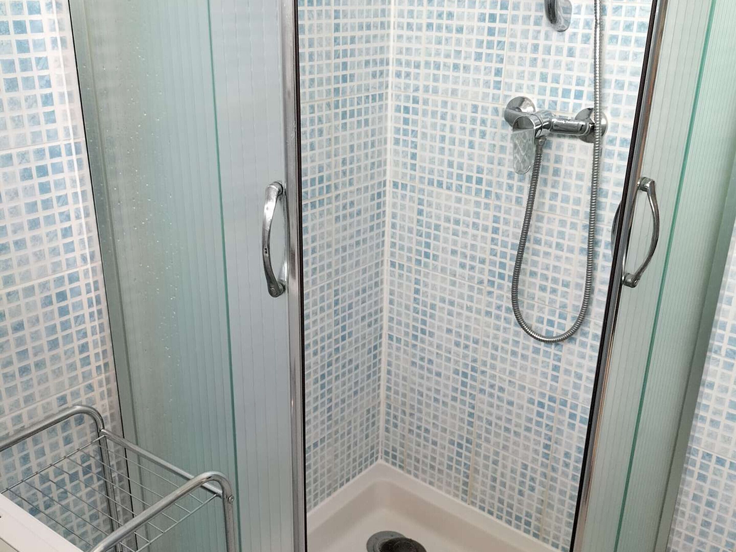 Una doccia con porta in vetro, soffione a mano e barra di sostegno in metallo.
