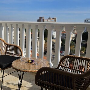 A balcony with wicker furniture, a glass table, and a view of buildings. - 104 NIC - 501 Stay Cosmo City Suite (Nicosia)