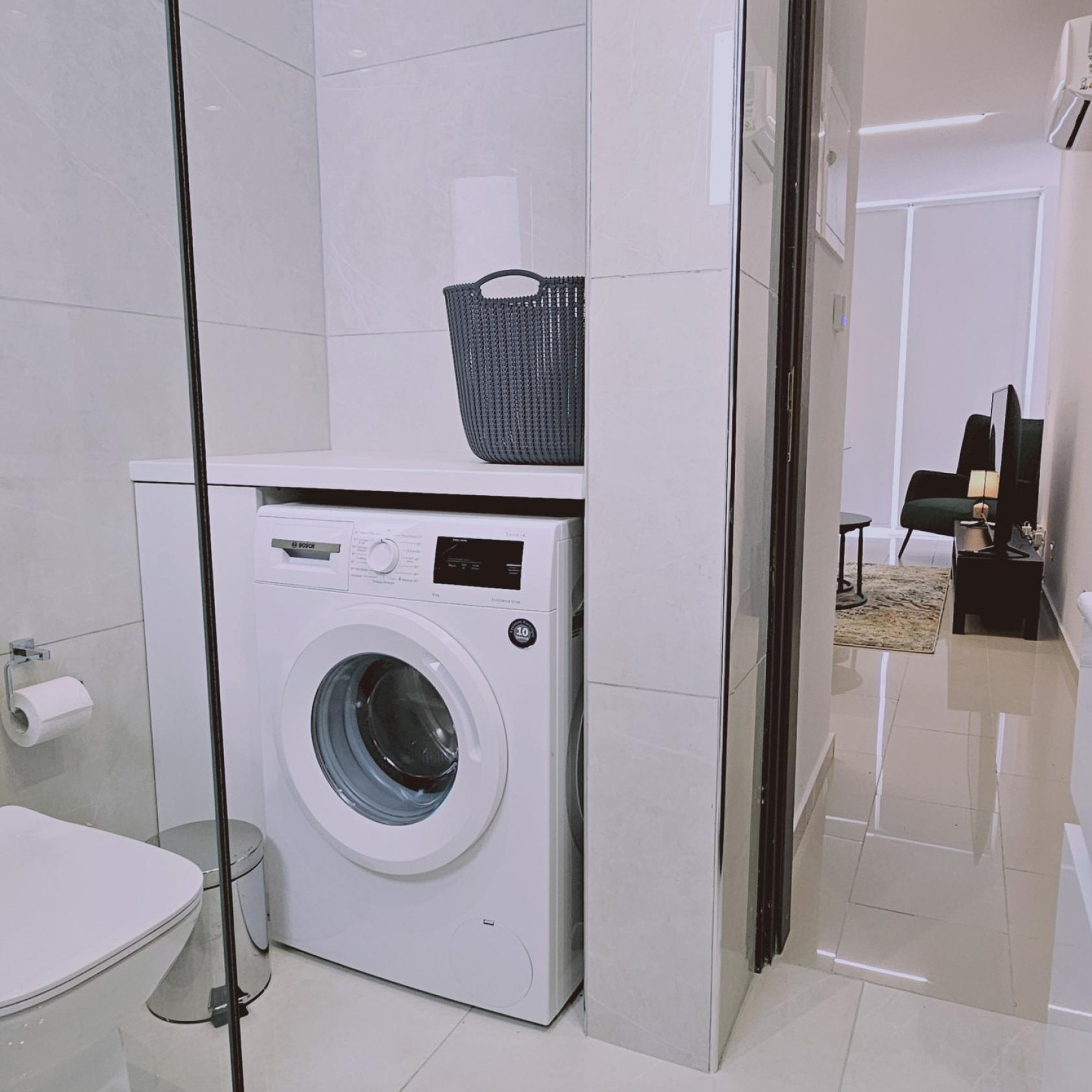 Un baño moderno con lavadora blanca, cabina de ducha de vidrio y un inodoro a la vista.