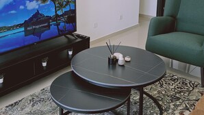 A modern living room with a large flat-screen TV on a black stand, a green armchair, and a round black coffee table with a small potted plant and a decorative item.