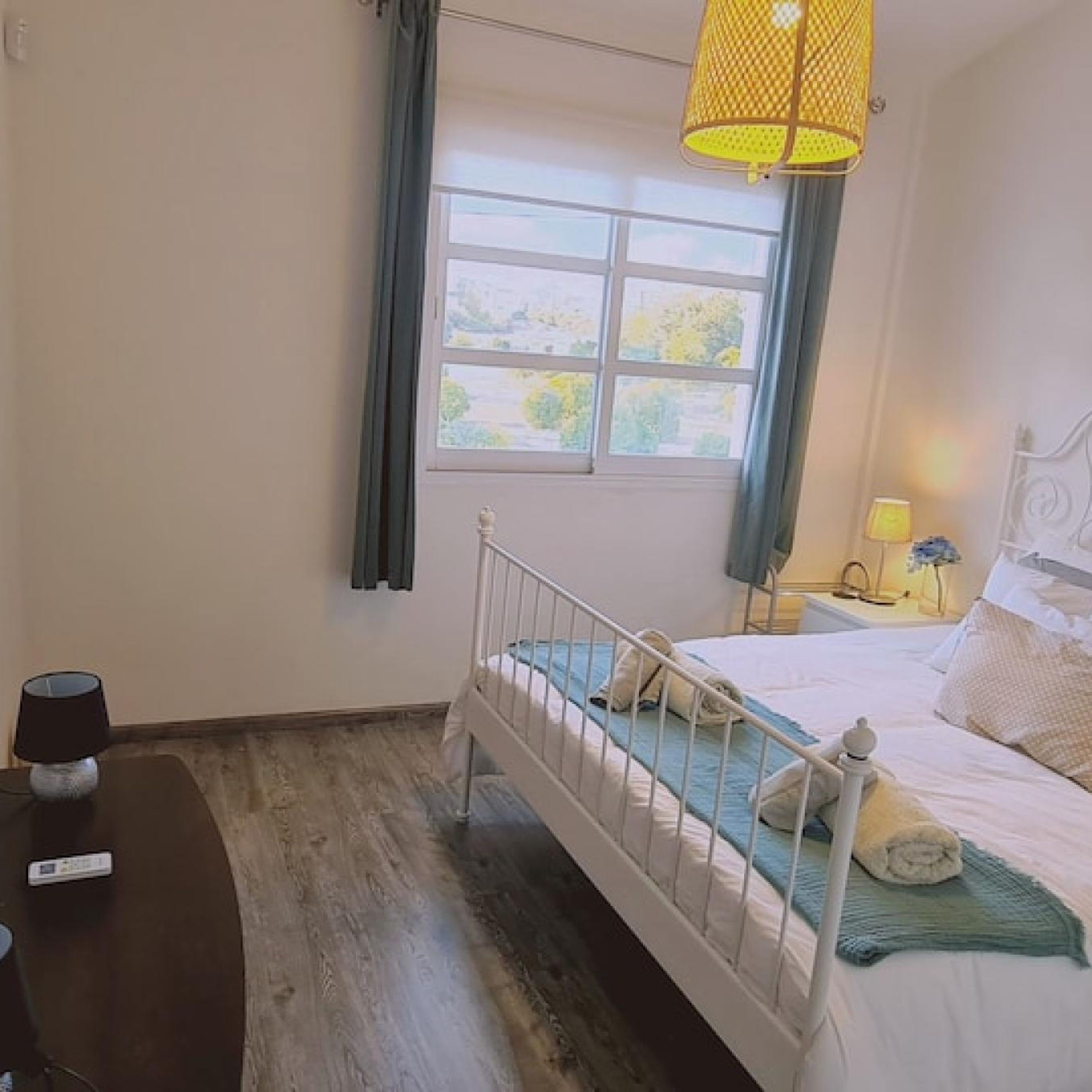 Une chambre avec un lit simple, une table de chevet, une lampe et une fenêtre avec des rideaux.