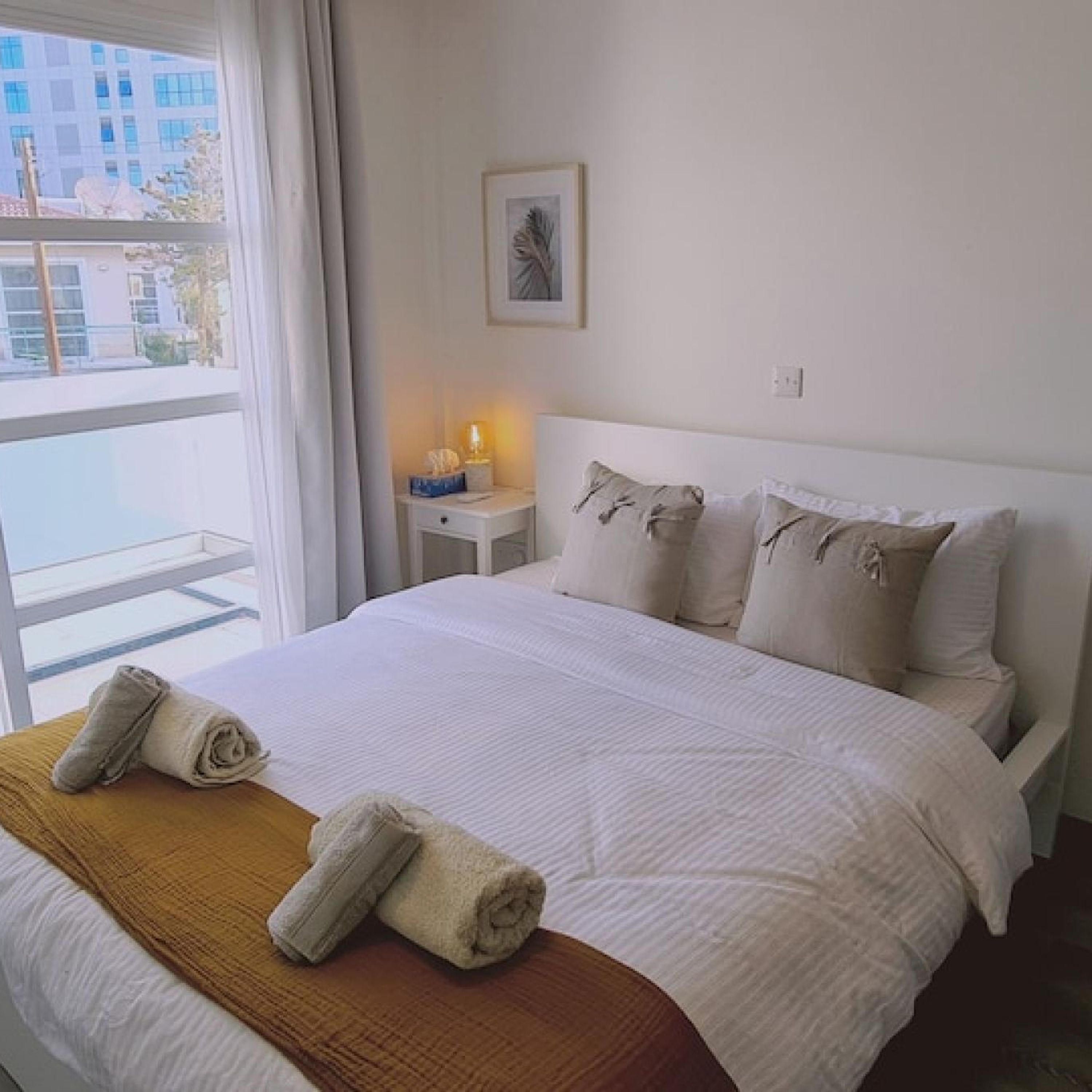 Hotelkamer met een groot bed, een nachtkastje met een lamp en een raam met uitzicht op gebouwen.