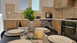 Une cuisine avec une table à manger dressée pour quatre personnes, un vase avec des plantes vertes, une bougie et un bol décoratif.