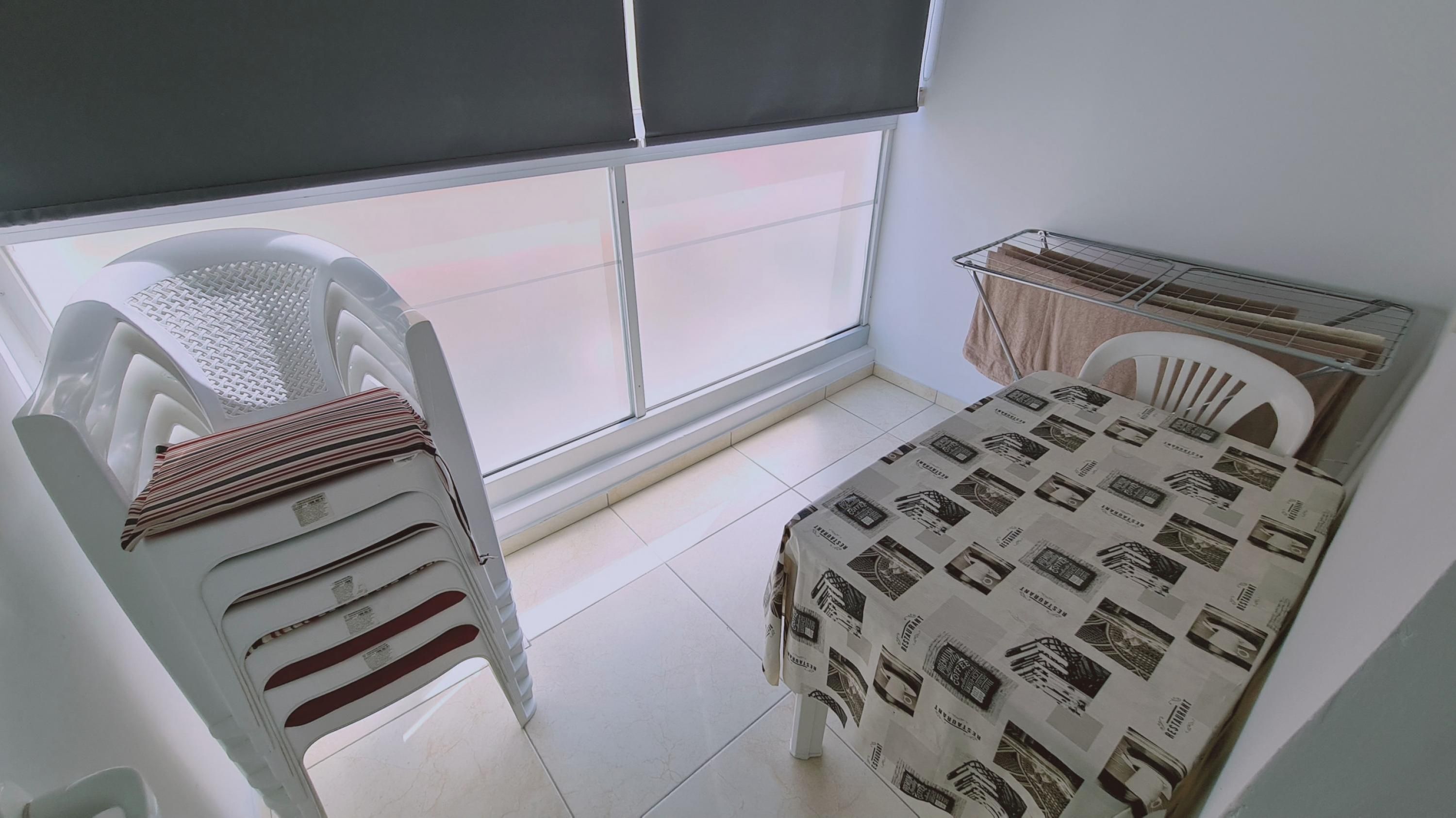 A small room with a bed, a chair, a table, and a window with blinds.