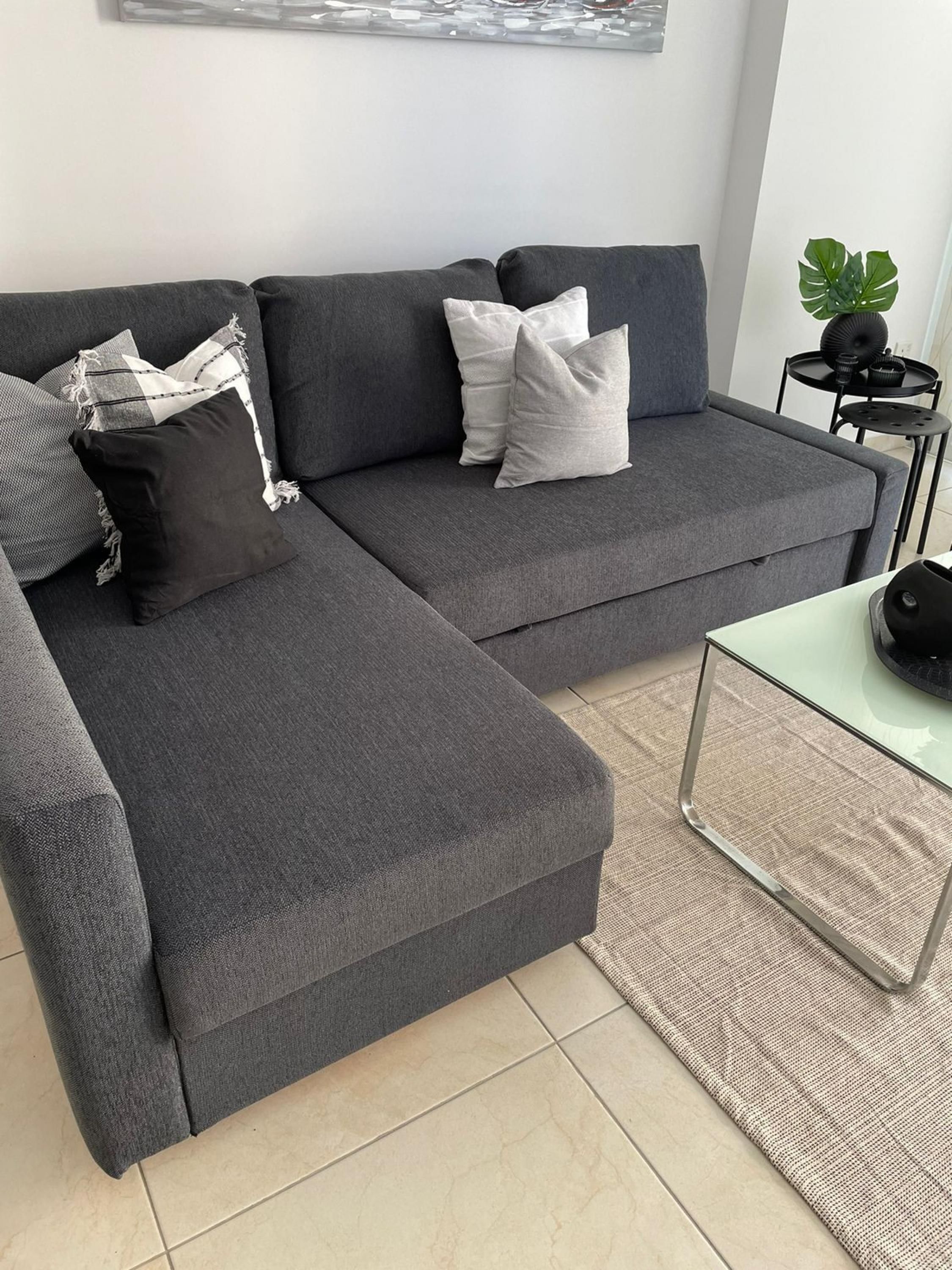 A grey sectional sofa with multiple pillows, a small side table with a plant, and a glass coffee table.