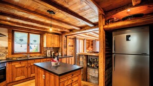 Eine Holzhüttenküche mit einer zentralen Kochinsel, Holzschränken, einem eingebauten Kamin aus Stein und einem Edelstahlkühlschrank.