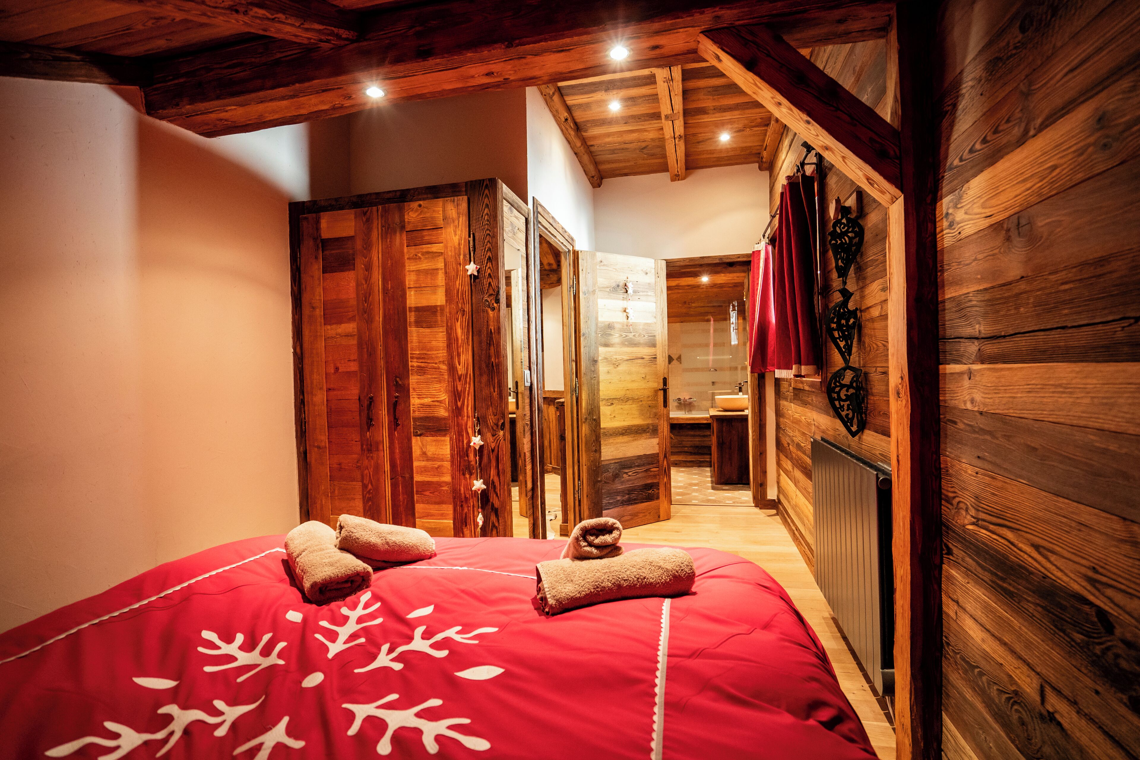 Une pièce avec un plafond en bois, un lit rouge orné de motifs blancs en forme de feuilles et une armoire en bois.
